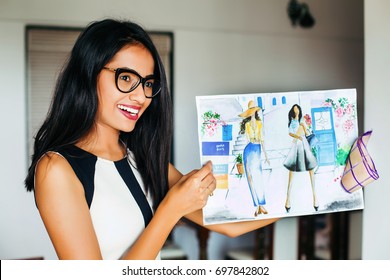 A Happy Young Female Indian Fashion Designer Showing Her Garment Designs On A Sheet