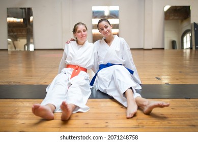 Happy young female karatekas sitting and hugging together. Cheerful Caucasian girls resting after karate class in studio. Sports, martial arts, healthy lifestyle concept - Powered by Shutterstock