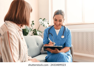 Happy young female nurse provide care medical service help support smiling mature woman at homecare medical visit, lady carer doctor give empathy encourage retired patient sit on sofa at home hospital - Powered by Shutterstock