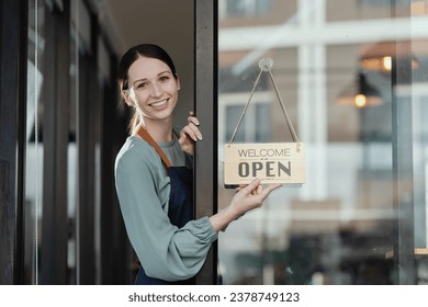 Happy young female owner standing with open sign at coffee shop, Smiling small business owner showing open sign.  - Powered by Shutterstock