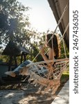 happy young female riding on macrame swing chair near country house outdoors