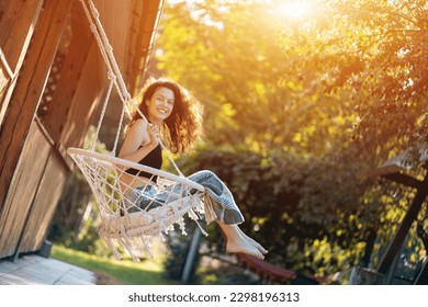 happy young female riding on macrame swing chair near country house outdoors - Powered by Shutterstock