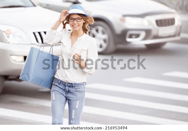 Happy\
young female student crossing the street with a coffee-to-go cup\
and tipping hat against urban city\
background.