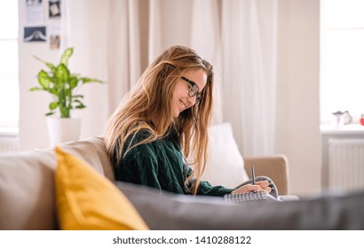 A Happy Young Female Student Sitting On Sofa, Studying.