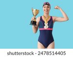 Happy young female swimmer with medals and gold cup showing muscle on blue background