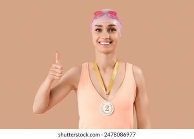 Happy young female swimmer with second place medal showing thumb-up on beige background - Powered by Shutterstock