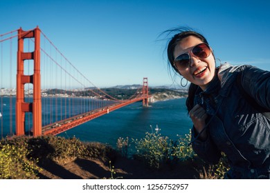 Happy young female tourists wearing sunglasses taking selfie in San Francisco by Golden Gate Bridge USA. asian woman face camera smiling attractive taking self portrait with famous attraction in us. - Powered by Shutterstock