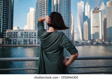 Happy young female traveler in the big city of Dubai, famous place Dubai marina. Luxury and comfortable tourism season in United Arab Emirates. Back or rear view of young woman in dress