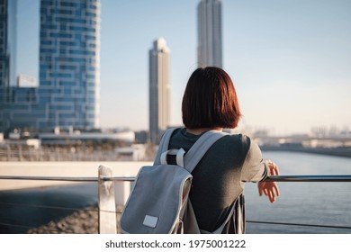 Happy young female traveler in the big city of Dubai, Blue Water Island. Luxury and comfortable tourism season in United Arab Emirates. Back or rear view of young woman in dress and backpack