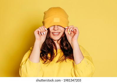 Fröhliche junge Weibchen auf trendigem gelbem Pullover und auf den Augen liegender Hut auf gelbem Hintergrund