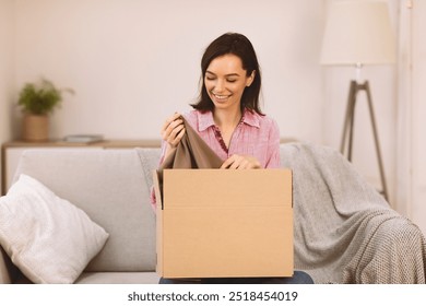 Happy young female volunteer sorting clothing donations in cardboard box, copyspace - Powered by Shutterstock