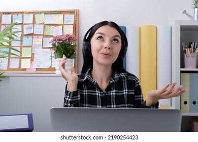 Happy young female wearing wireless headphones is looking up, holding conversation with clients online, working remotely at the workplace from home office. - Shutterstock ID 2190254423