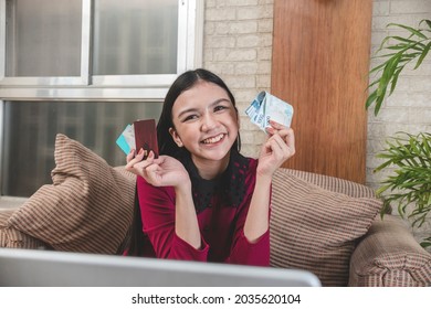 A happy young Filipina lady holding a few credit cards and a handful of 1000 peso bills while at the couch. Ready for a shopping spree experience. - Shutterstock ID 2035620104