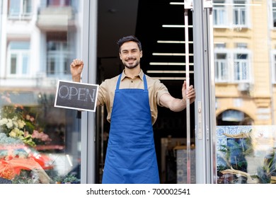 happy young florist in apron holding open sign and smiling at camera - Powered by Shutterstock