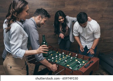 Happy young friends drinking beer and playing foosball indoors