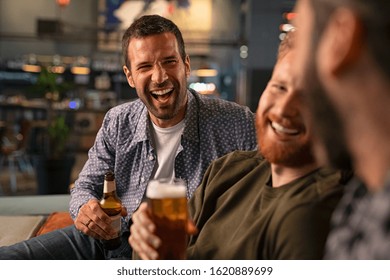 Happy young friends drinking draft beer while having fun in pub and laughing. Group of mid adult smiling men drinking beer and talk in bar while sitting on couch. guys celebrating bachelor party. - Powered by Shutterstock