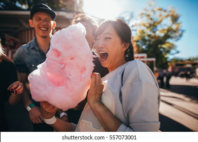 Happy young friends eating cotton candy outdoors. Young man and women with cotton candy floss at fairground.