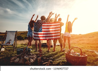 Happy young friends enjoy a sunny day in nature. They're looking at sun holding american flag and greeting, happy to be together. - Powered by Shutterstock