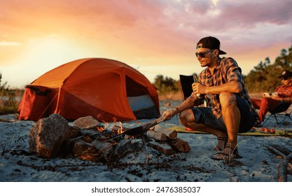 Happy young friends enjoy a sunny day at the nature. They're toasting with beer bottles by the bonfire near tent. - Powered by Shutterstock