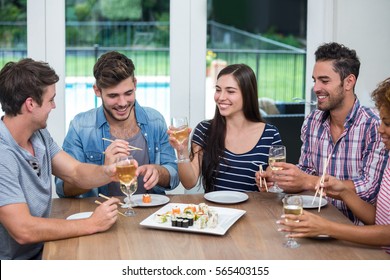 Happy young friends enjoying wine and sushi at table in house - Powered by Shutterstock