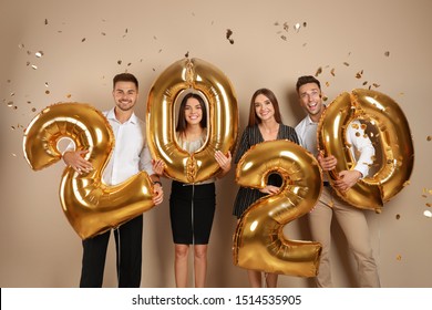 Happy Young Friends With Golden 2020 Balloons On Beige Background. New Year Celebration