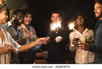 Happy young friends having fun with sparklers fireworks and drinking cocktails on house patio party - Youth people lifestyle and holidays concept