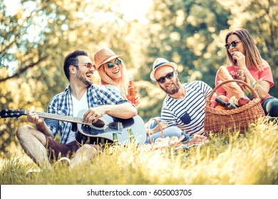Happy young friends having picnic in the park.They are all happy,having fun,smiling and playing guitar.
