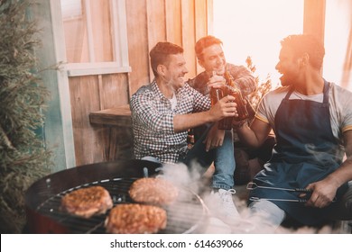 happy young friends making barbecue and drinking beer on porch with back light - Powered by Shutterstock