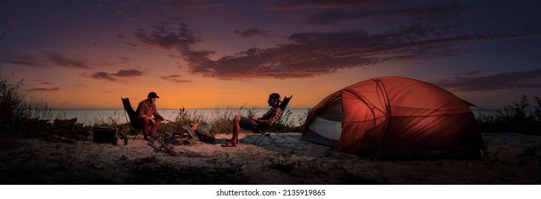 Happy Young Friends Resting By The Bonfire Near Tent.