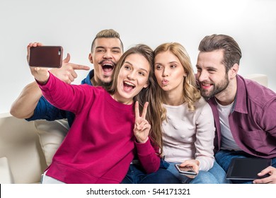 Happy Young Friends Taking Selfie While Sitting On Couch Isolated On White