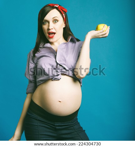 Happy young funny pregnant woman in pin up style holding apple in her hand
