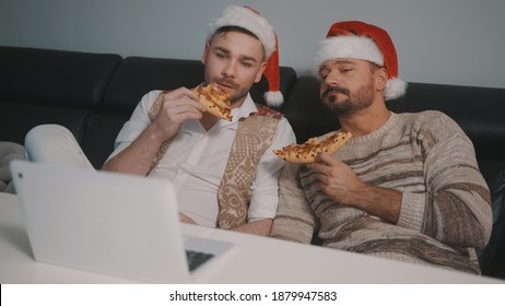 Happy Young Gay Couple With Santa Claus Hats Watching Movies On The Laptop And Eating Pizza On The Christmas Eve. High Quality Photo