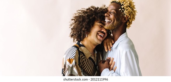 Happy Young Gay Couple Standing Together In A Studio. Two Affectionate Male Lovers Smiling Cheerfully While Embracing Each Other Against A Studio Background. Young Gay Coupe Being Romantic.