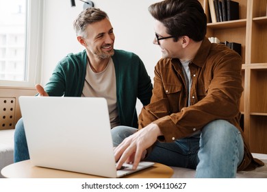 Happy Young Gay Couple Using Laptop Computer While Sitting On A Couch At Home