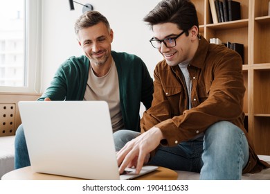 Happy Young Gay Couple Using Laptop Computer While Sitting On A Couch At Home