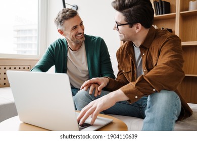 Happy Young Gay Couple Using Laptop Computer While Sitting On A Couch At Home