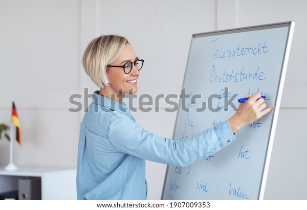 Happy young\
German tutor writing grammar rules on blackboard, giving online\
lesson from home. Friendly foreign languages teacher explaining new\
material to students on\
web