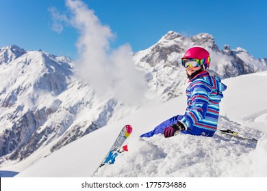 Happy Young Girl In Bright Sport Outfit Sit On The Snow Pile In The Mountain Over High Peaks Look Back To Camera