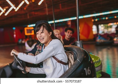 Happy young girl driving a bumper car with friends in background at amusement park