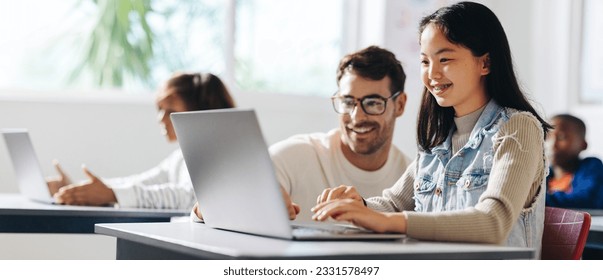 Happy young girl getting assistance from her teacher as she engages in a computer science lesson. Female student learning and understanding the basics of digital literacy in a classroom. - Powered by Shutterstock