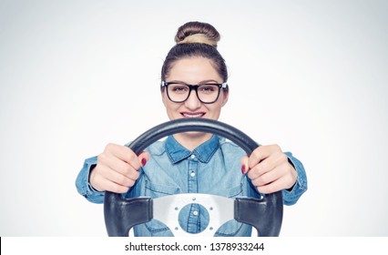 Happy young girl with glasses and car steering wheel, front view, auto concept 