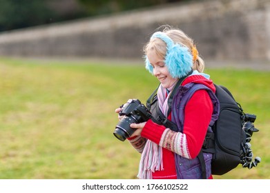 A Happy Young Girl Holding A Camera And Wearing Blue Ear Muffs.