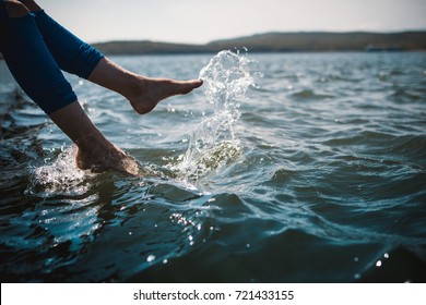 A happy young girl is kicking feet on a sea pier and splashing water