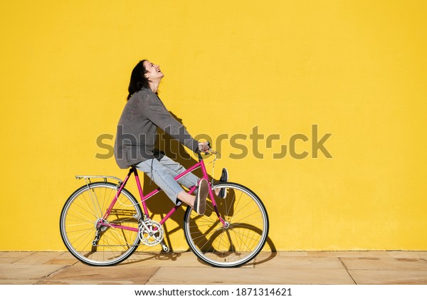 happy young girl laughs as\
she plays on her retro pink bike next to a colorful yellow wall,\
concept of active lifestyle and sustainable mobility, copy space\
for text