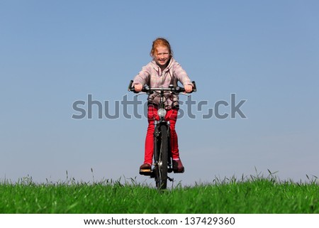 Happy young girl on bike on green meadow