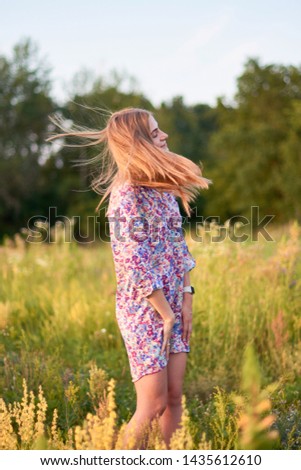 A happy young girl on a flowering field at sunset