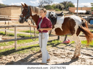 Happy young girl preparing horse for riding and walking in pasture on small farm - Powered by Shutterstock