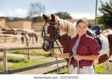 Happy young girl preparing horse for riding and walking in pasture on small farm - Powered by Shutterstock