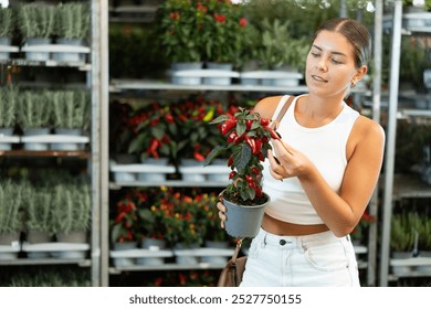 Happy young girl purchaser holding decorative pepper in garden-pot in flowers market - Powered by Shutterstock