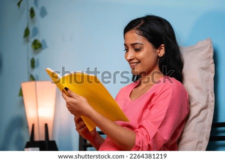 Happy young girl reading book or novel on bed before sleeping at home - concept of hobbies, knowledge and leisure activity.
